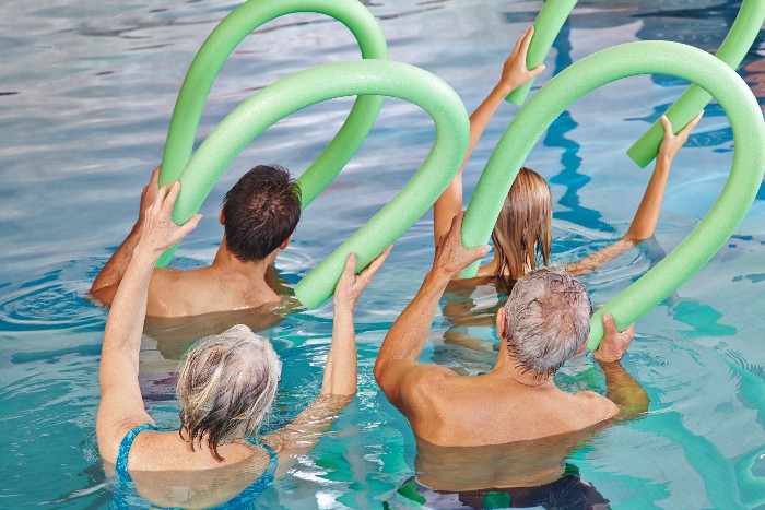Older people exercising with swim noodle in a pool
