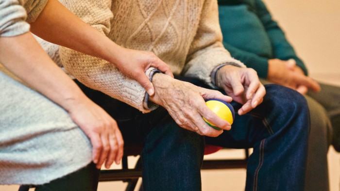 Elderly hands holding a stress ball with younger hands holding wrist in comfort