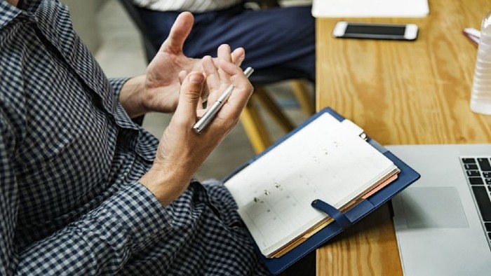 A man gesturing with hands in a meeting with notebook and laptop