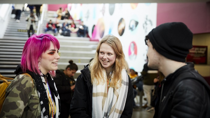 Two female students speaking to a male student