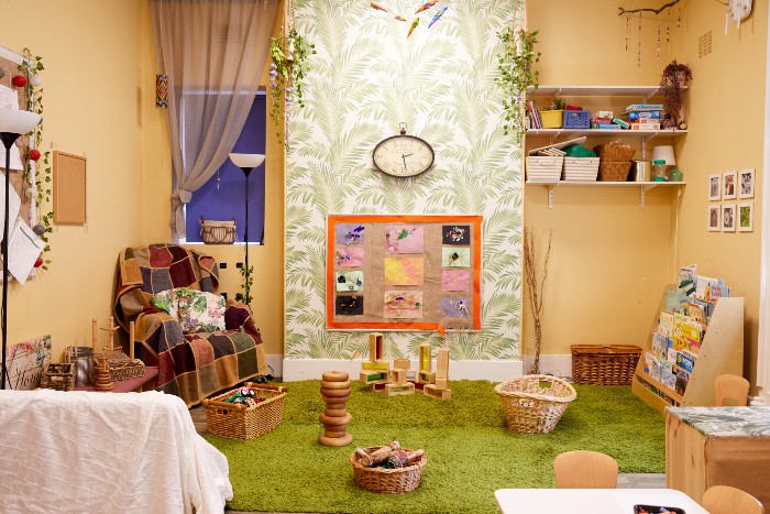 One of the playrooms in the nursery. There is a an armchair in the left corner of the room, a bookshelf to the right and a green carpeted area in between