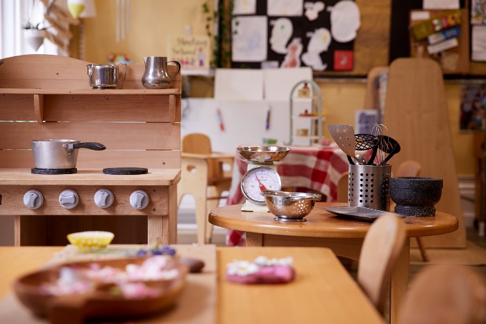 Children's play kitchen in the nursery with a wooden stovetop, a table full of utensils and a dining table