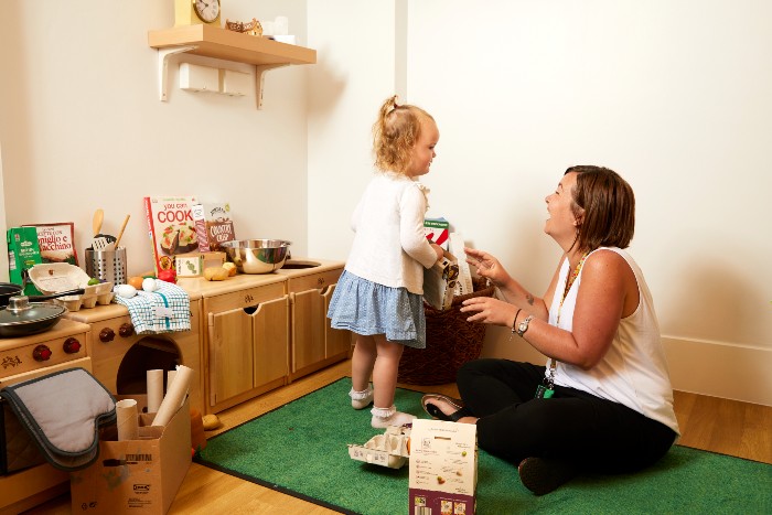A member of nursery staff playing with a child in a wooden kitchen