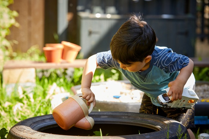 A little boy with a watering can in the meadows garden waters soil in a tire planter
