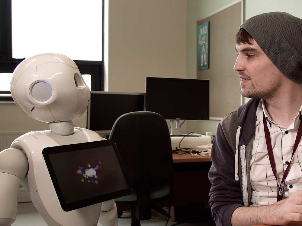 Student wearing a beanie hat talking to a white human robot.
