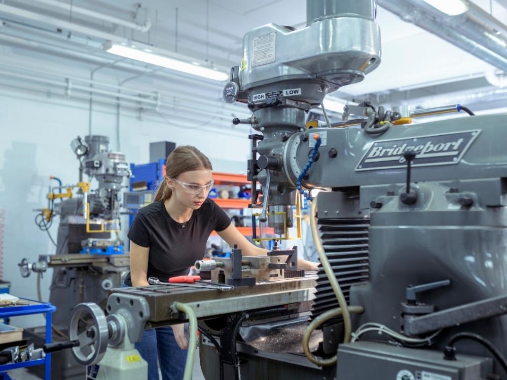 A student is using heavy equipment in a mechanical engineering workshop.
