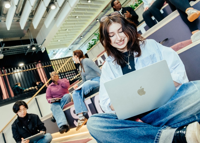 A group of students sat on a set of steps on campus, working from laptops and in casual discussion.