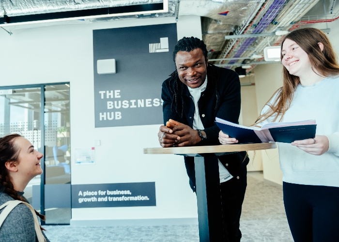 A group of three people talking around a tall table in a Sheffield Hallam campus business hub.