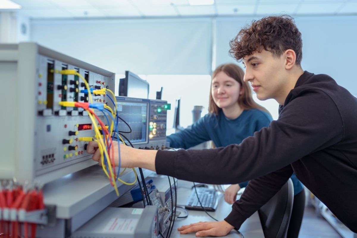 Two students are working on electronic equipment in a brightly lit workshop space.
