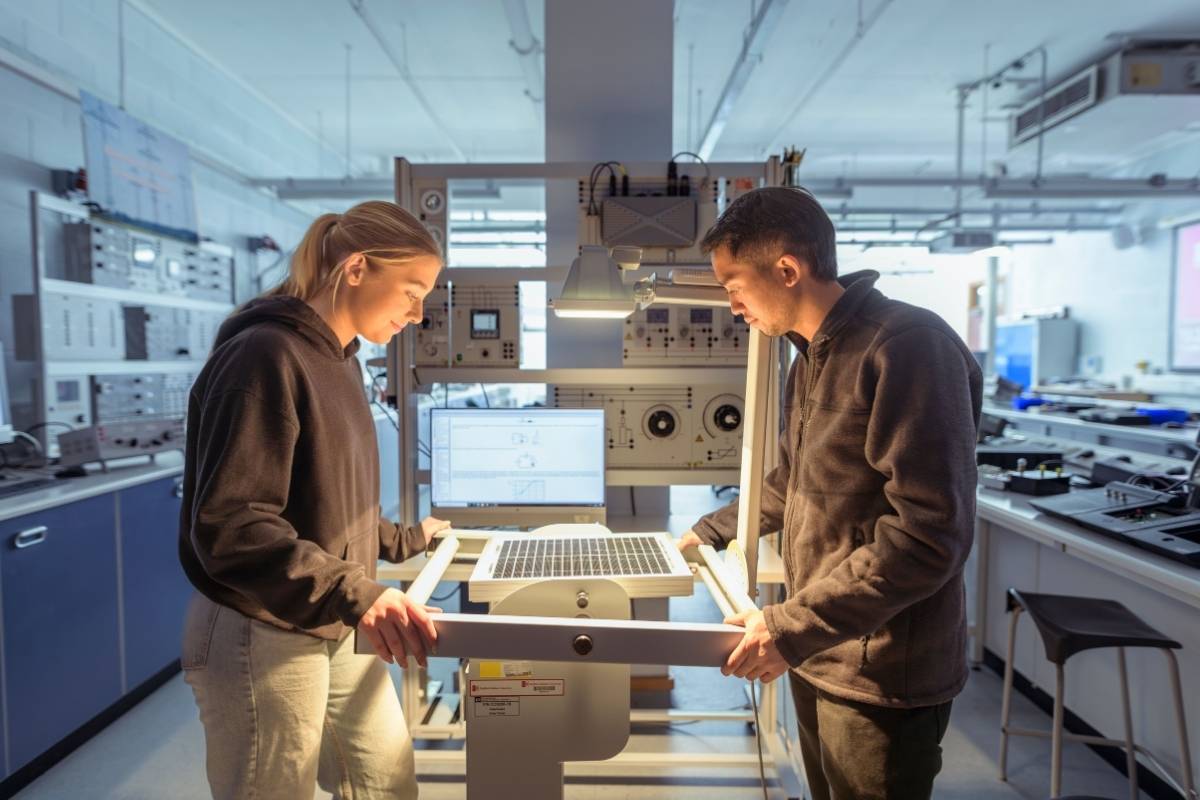 A student and tutor are stood looking over a piece of electrical equipment they're holding.