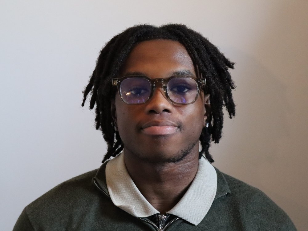 Head and shoulders shot of student Andrew, who is wearing glasses and a white polo shirt under a grey jumper.
