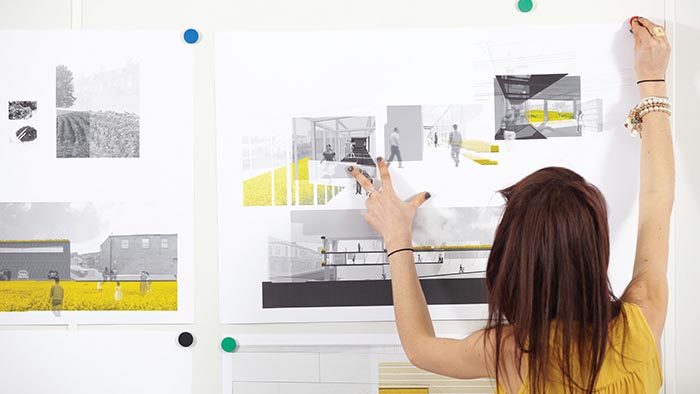 A student pinning architectural designs on a wall