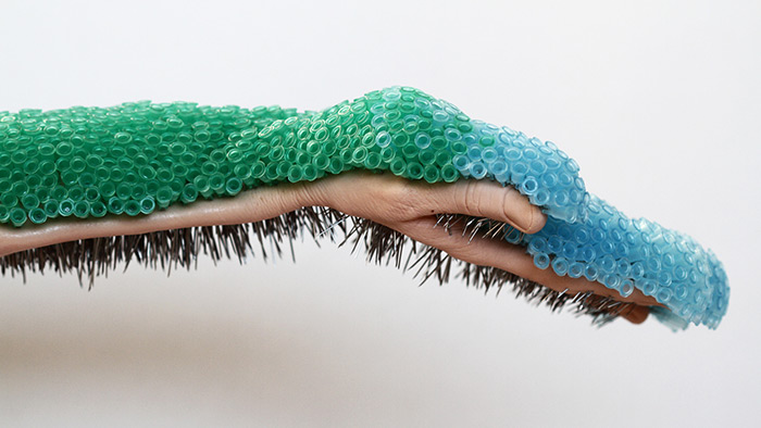 A sculpture of an upturned hand and forearm, with a dense layer of green and blue bubbles covering the upper side and thick, wiry hair emerging from the lower.
