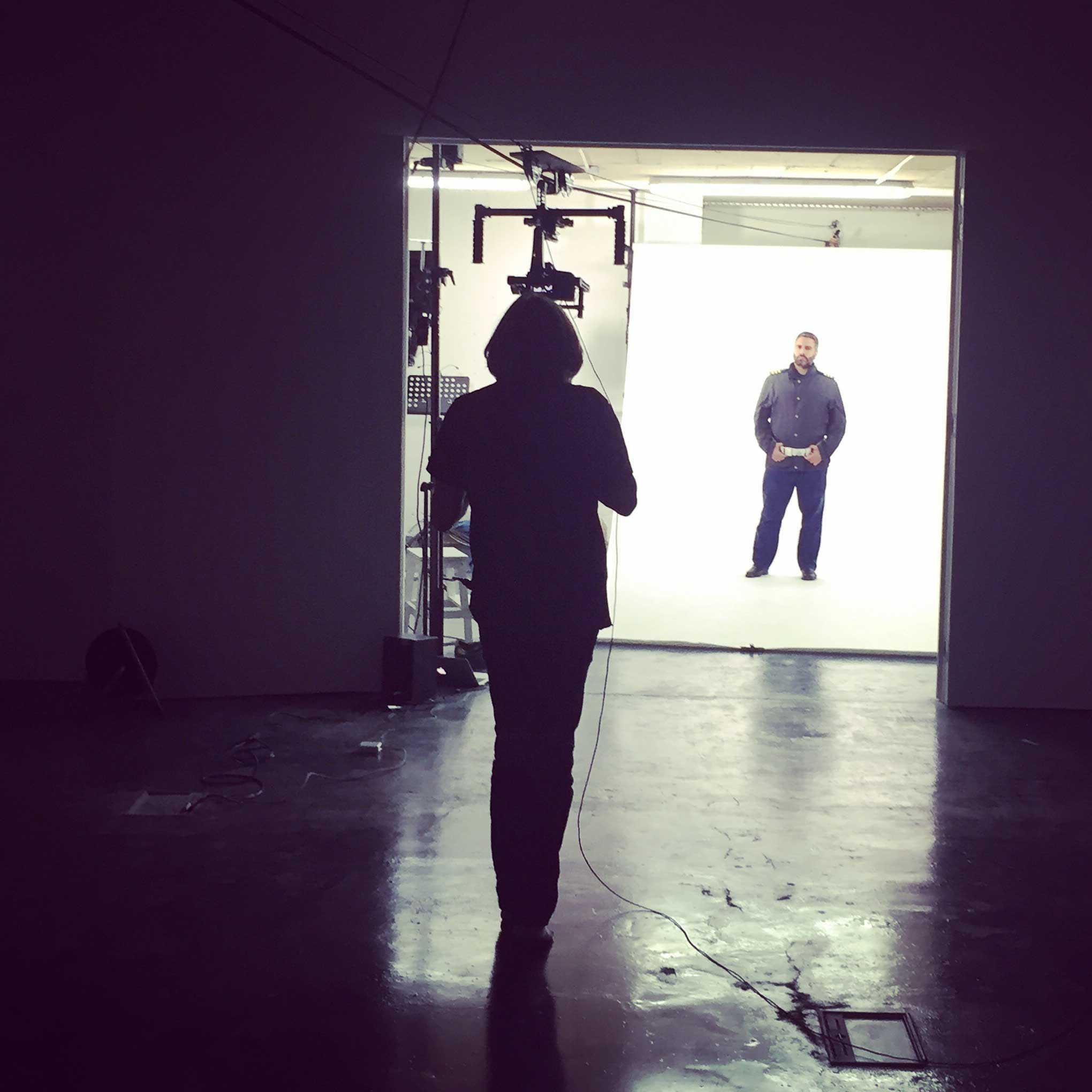 Production image of Mirror II by David Cotterrell - A man is standing in front of a white screen recording for the piece. David Cotterrell is in the foreground.
