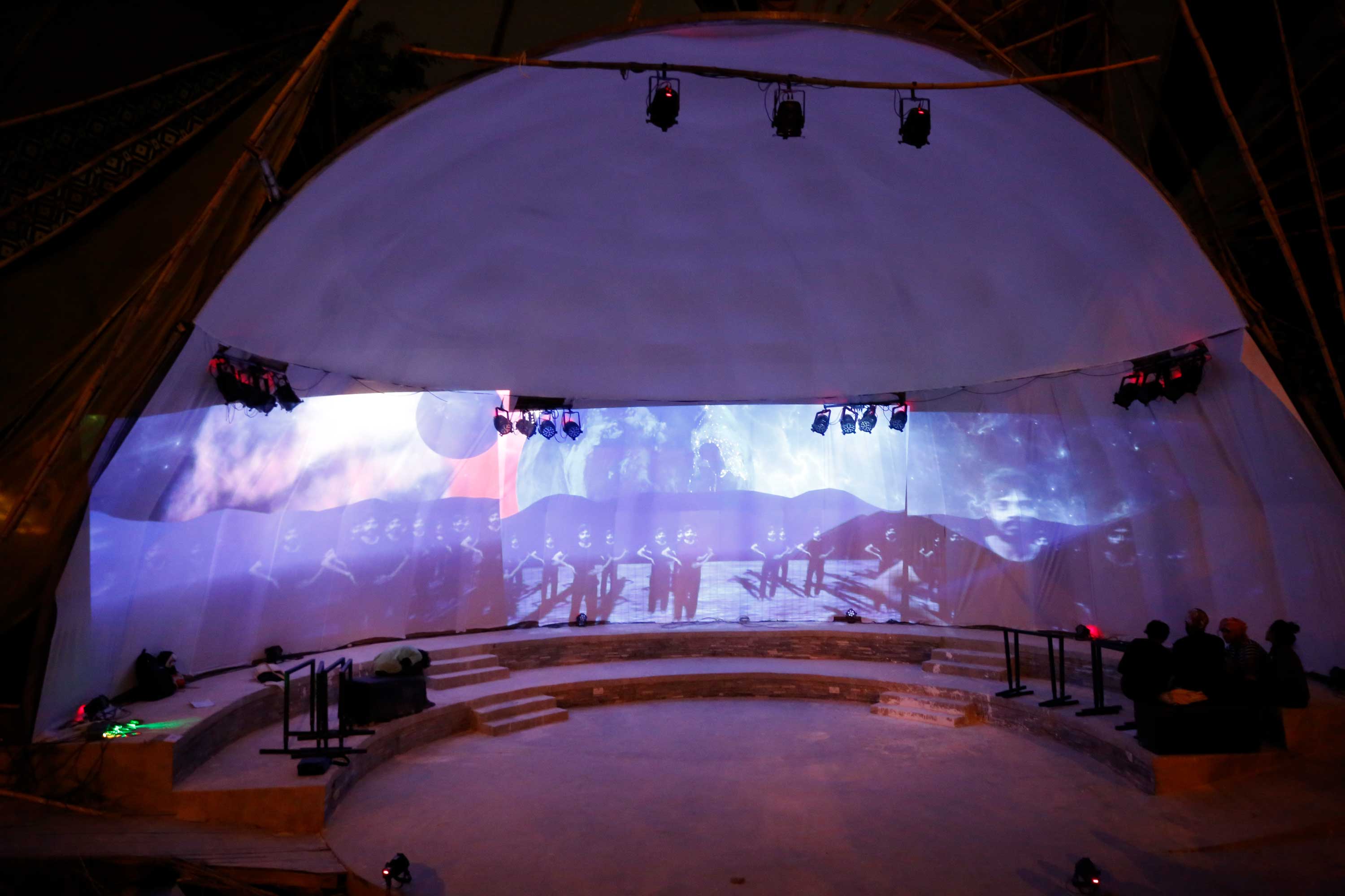Performance image of Thought Curfew by David Cotterrell. A dome-shaped stage has videos displayed on the back wall.