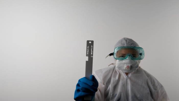 A person in a hazmat suit and goggles holding a piece of measuring equipment 
