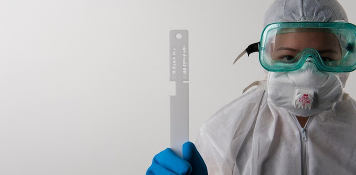 A close up image for a person wearing a hazmat suit with a piece of measuring equipment 
