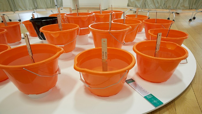 A table filled with orange buckets. The buckets have beach and a measuring stick in