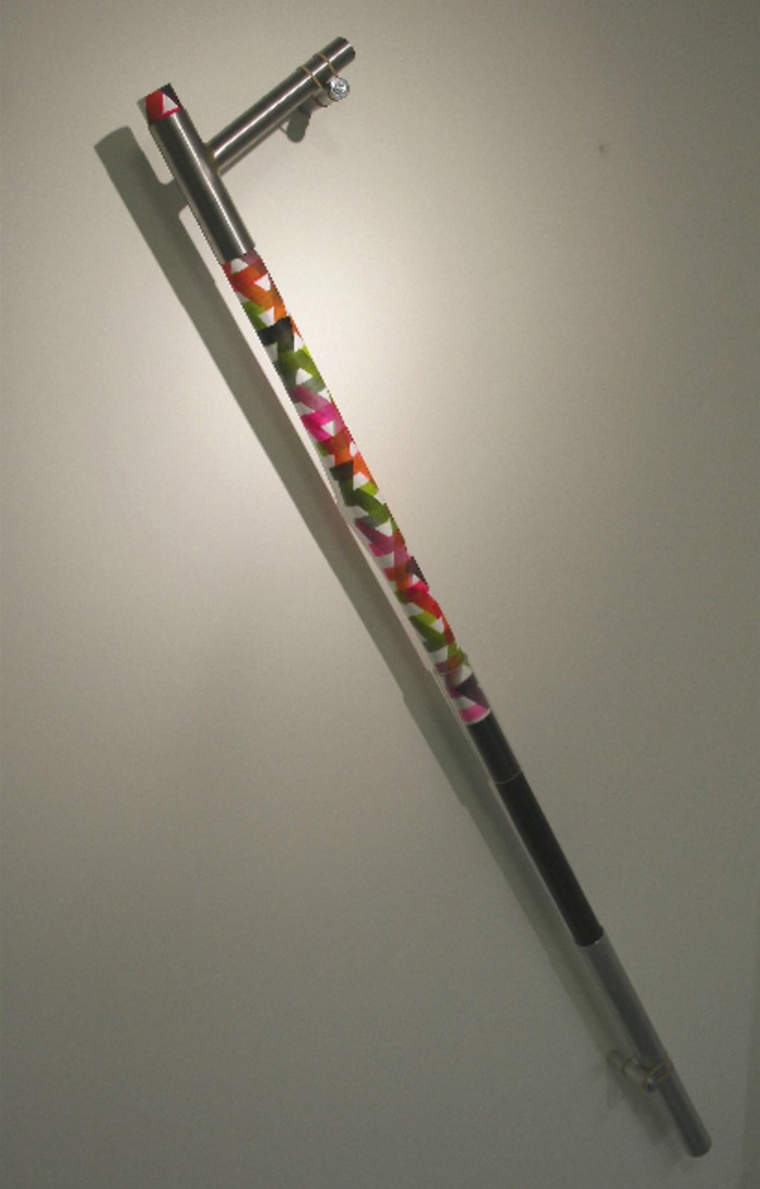 A metal bar covered with a multicoloured lattice pattern on a white background. It is topped with a small piece of metal that is perpendicular to the main piece
