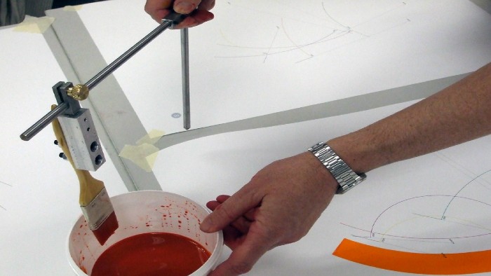 A person mixing paint in a bucket over a series of drawings