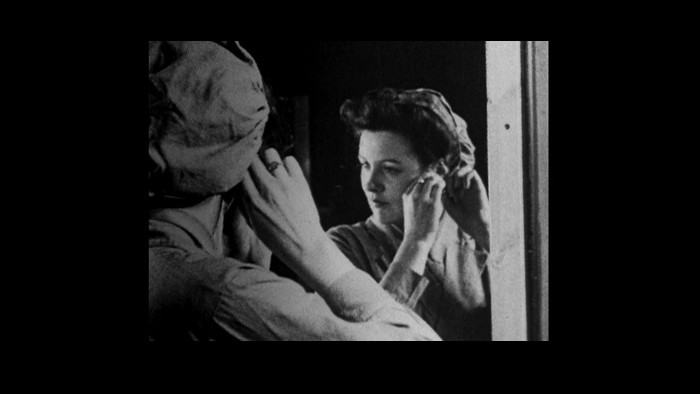 A still from the From Scotland with Love film. A woman puts on her earring whilst looking in the mirror.
