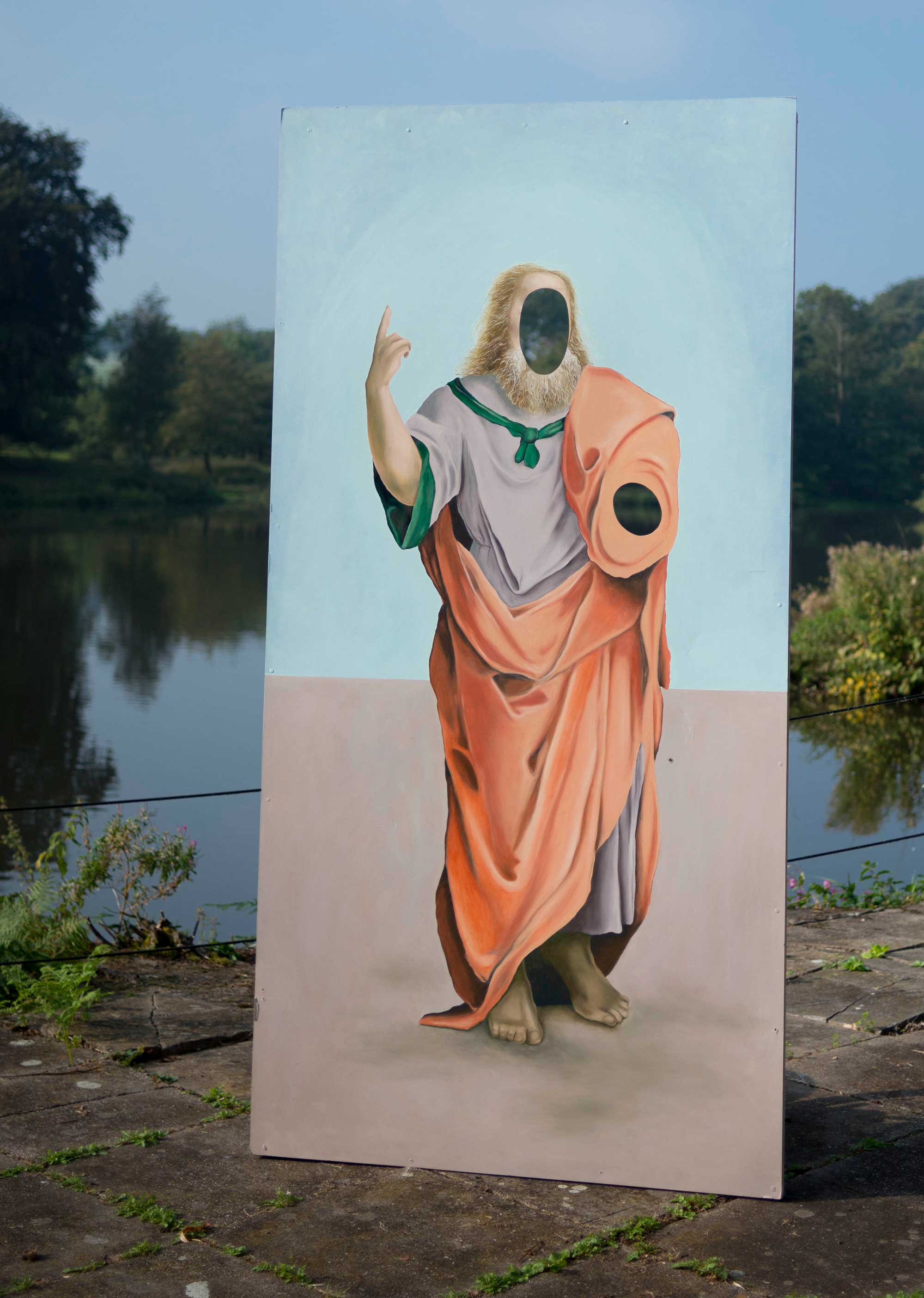 A large/life-size painting of a philosopher next to the lake of Yorkshire Sculpture Park. There are holes where the head and left arm are.