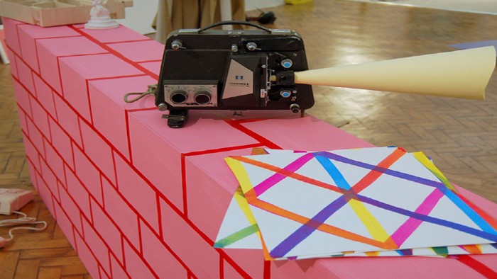 A piece of art from the Pile exhibition. An old radio sits on a pink and red wall with patterned paper