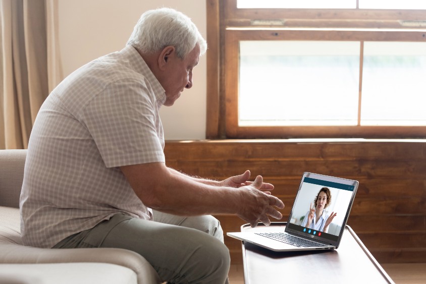 Man on sofa talking to clinician via laptop