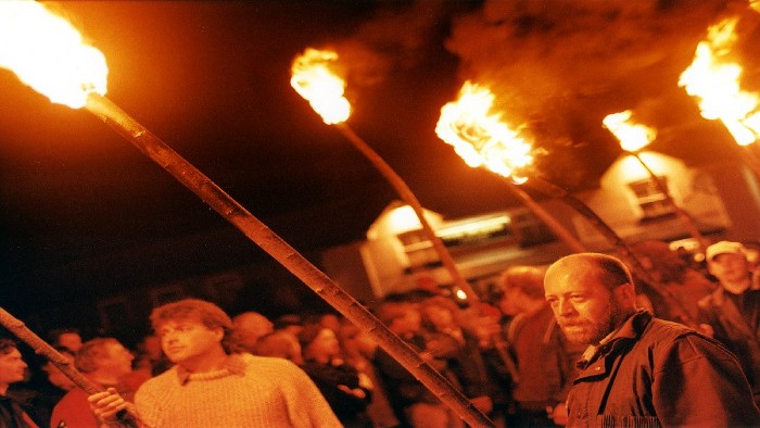 A 'mob' of people outside a building in the dark holding fire torches
