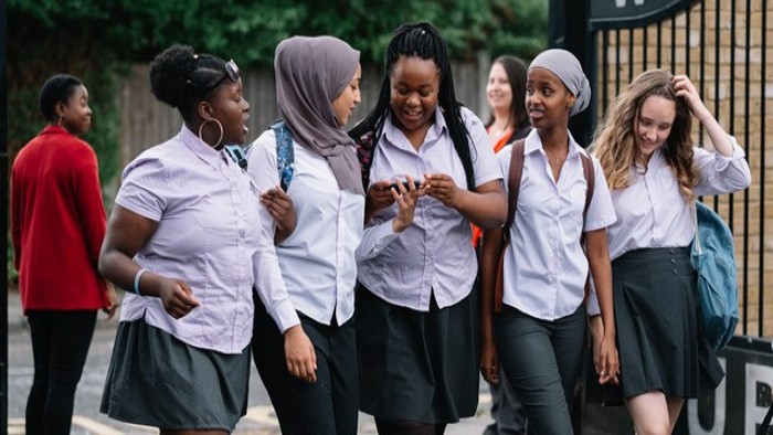 A group of 5 school girls of different ethnicities walking in a line talking