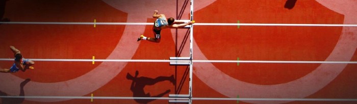 Athlete jumping over a hurdle on an Olympic track.