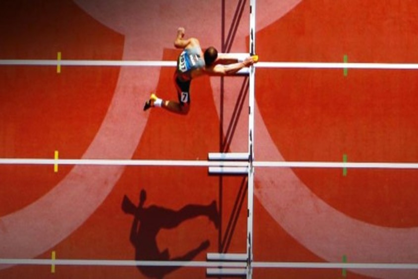 Athlete jumping over hurdles on an Olympic track.