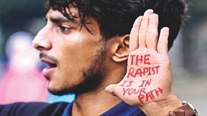 A man with a sign on his hand saying 'the rapist is in your path'