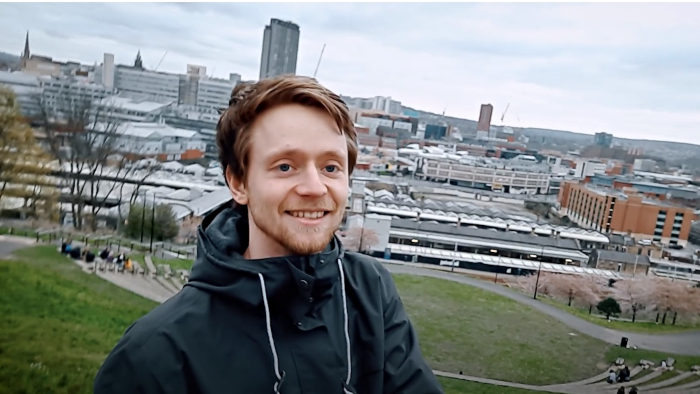 Daniel is wearing a grey hoodie with the Sheffield skyline in the background.