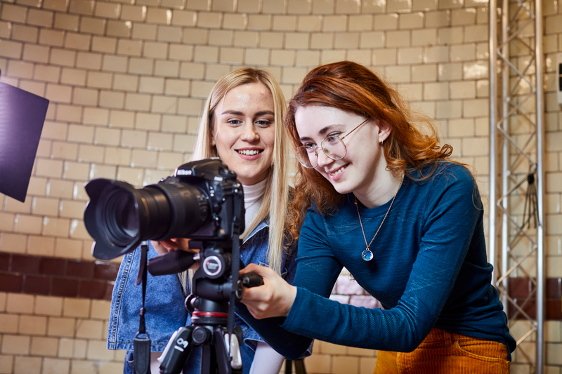 Two women are crouched by a camera and adjusting the settings