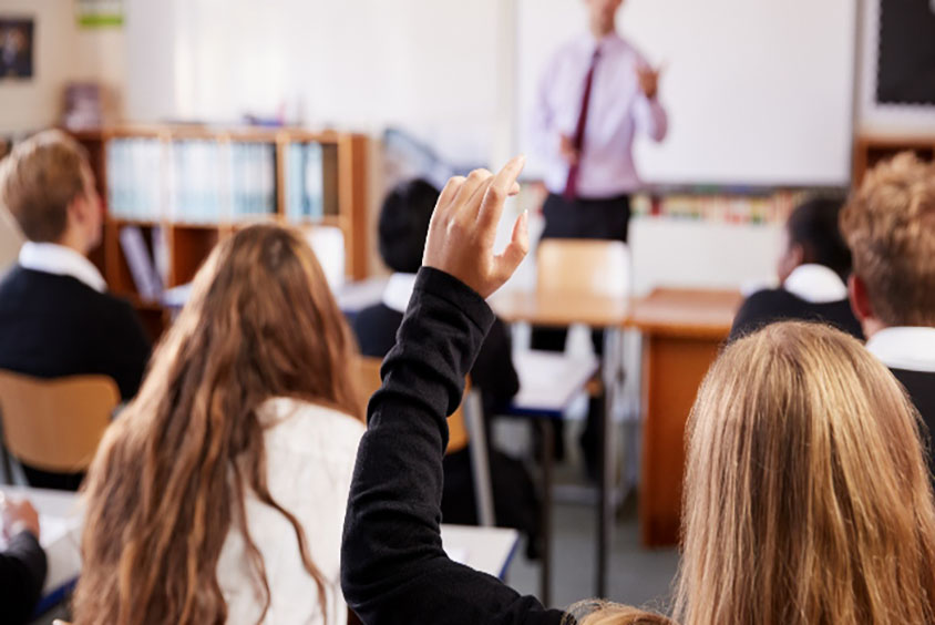 Child with raised hand in classroom to get teachers attention