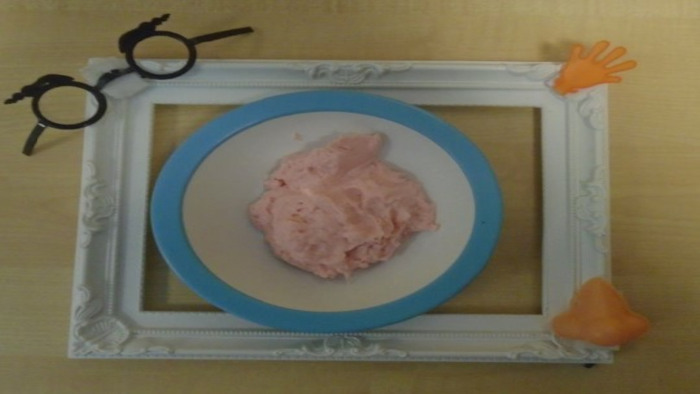 The image is a plate of food inside a frame which has a pair of glasses, a small toy hand and fake nose attached to it.