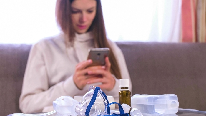 A nebuliser and medicine on a table, and a woman holding a mobile phone in the background