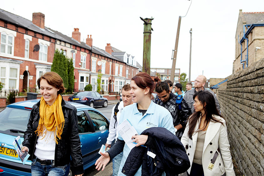 Several people in conversation on a guided waking tour down a terraced residential street.