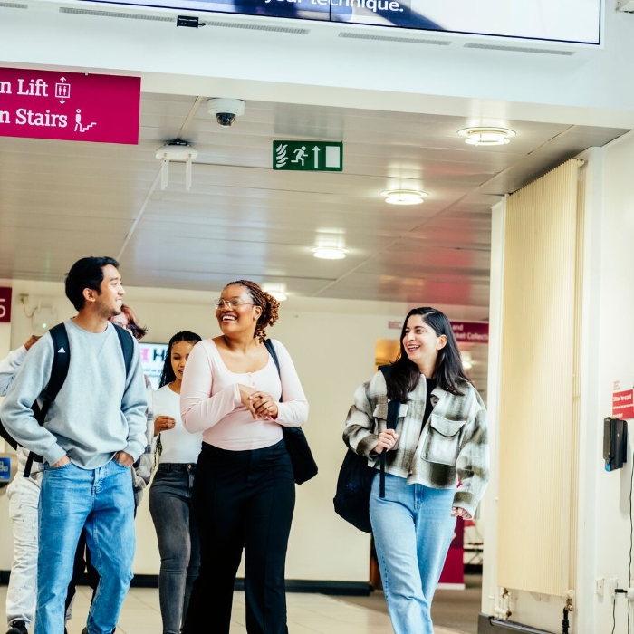 Three students walking through a university building, smiling and chatting.