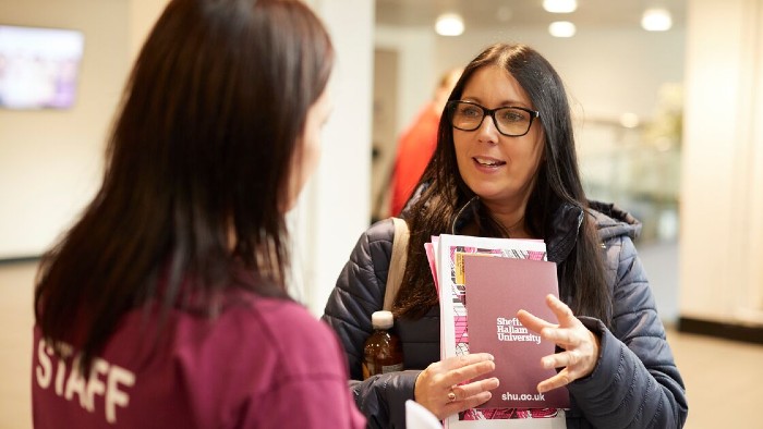 An open day attendee holding a guidebook and in discussion with a member of Sheffield Hallam staff