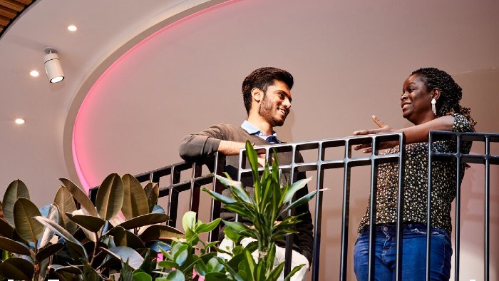 Two students stood talking on a balcony overlooking the atrium