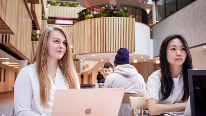 Two students sat at a table working from laptops in the City Campus atrium