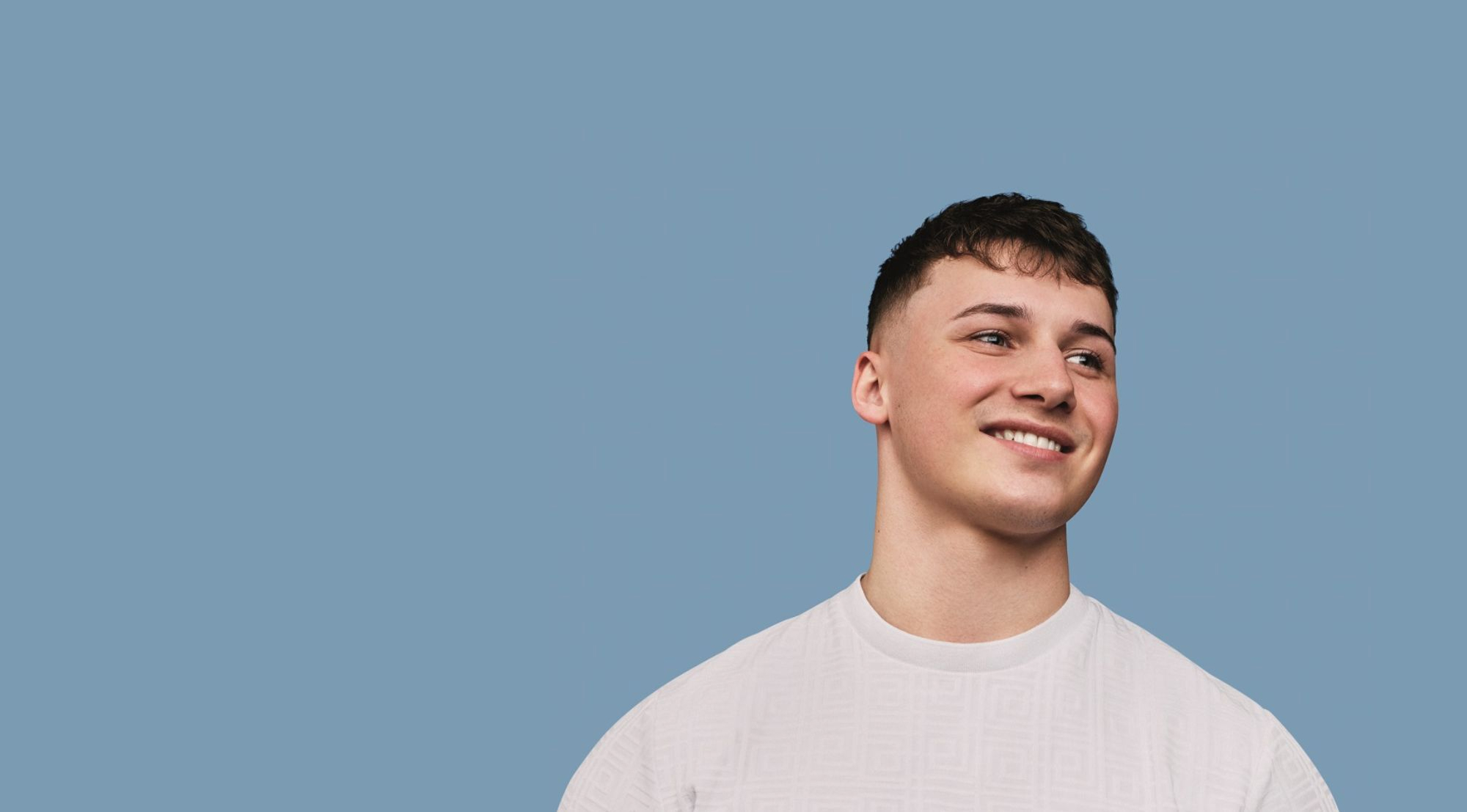 A person wearing a white shirt standing against a solid blue background and smiling.