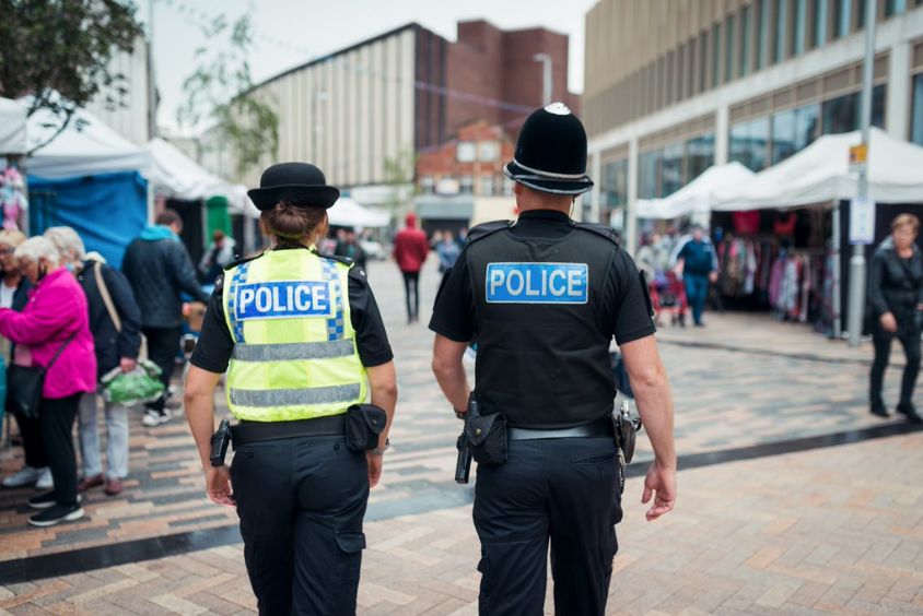 One female and one male police officers patrol a market street in uniform (back to camera).