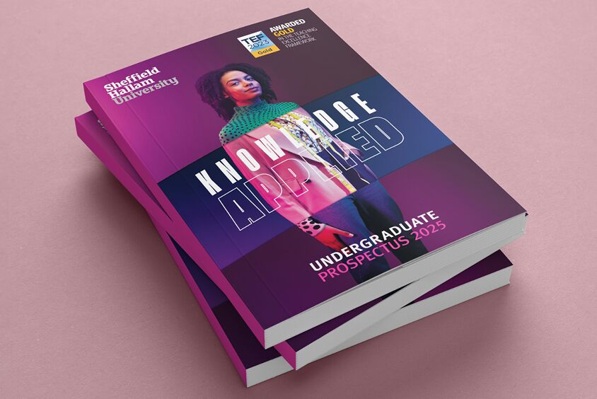 A thumbnail image of a stack of university prospectus showing an image of a women on the cover and a pink background
