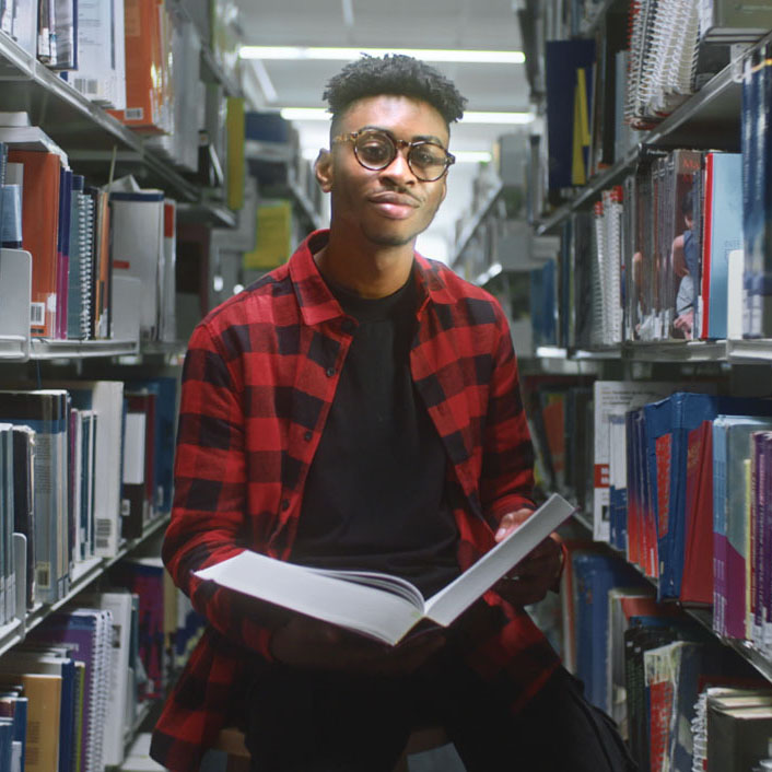 Student standing in the library with an open book