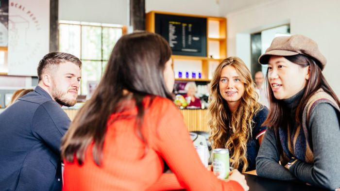 Four people sit around a table in a Sheffield Hallam cafe with a menu board and shelves in the background. One person is holing a can of drink.