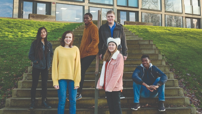 Group of students standing and sitting on steps in front of a building