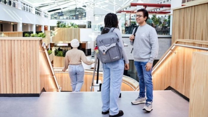 Two students standing chatting at the top of a flight of stairs in an open air atrium